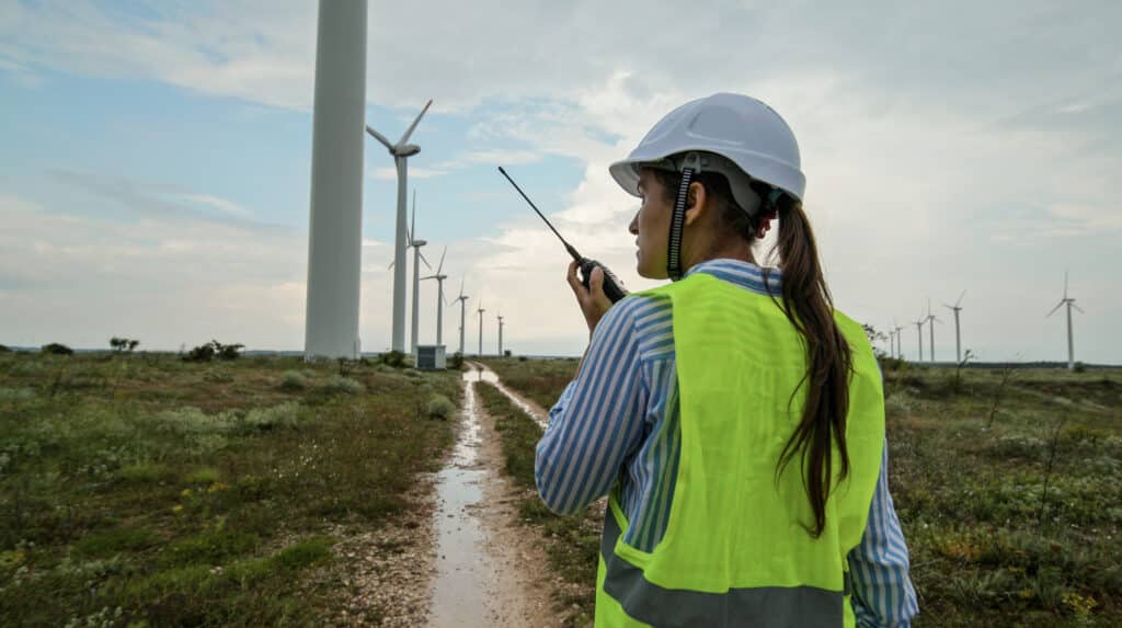 Electrical maintenance engineer working for the energy industry, supervising the condition of the power equipment in a wind turbines power station on a rainy day. Checking the data and the results of measurements with digital tablet.